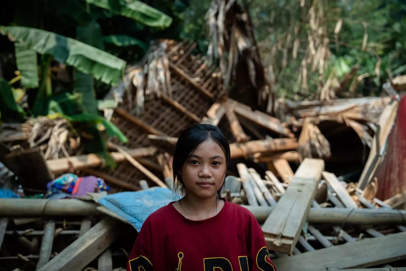 A young Vietnamese girl stands in front of rubble.