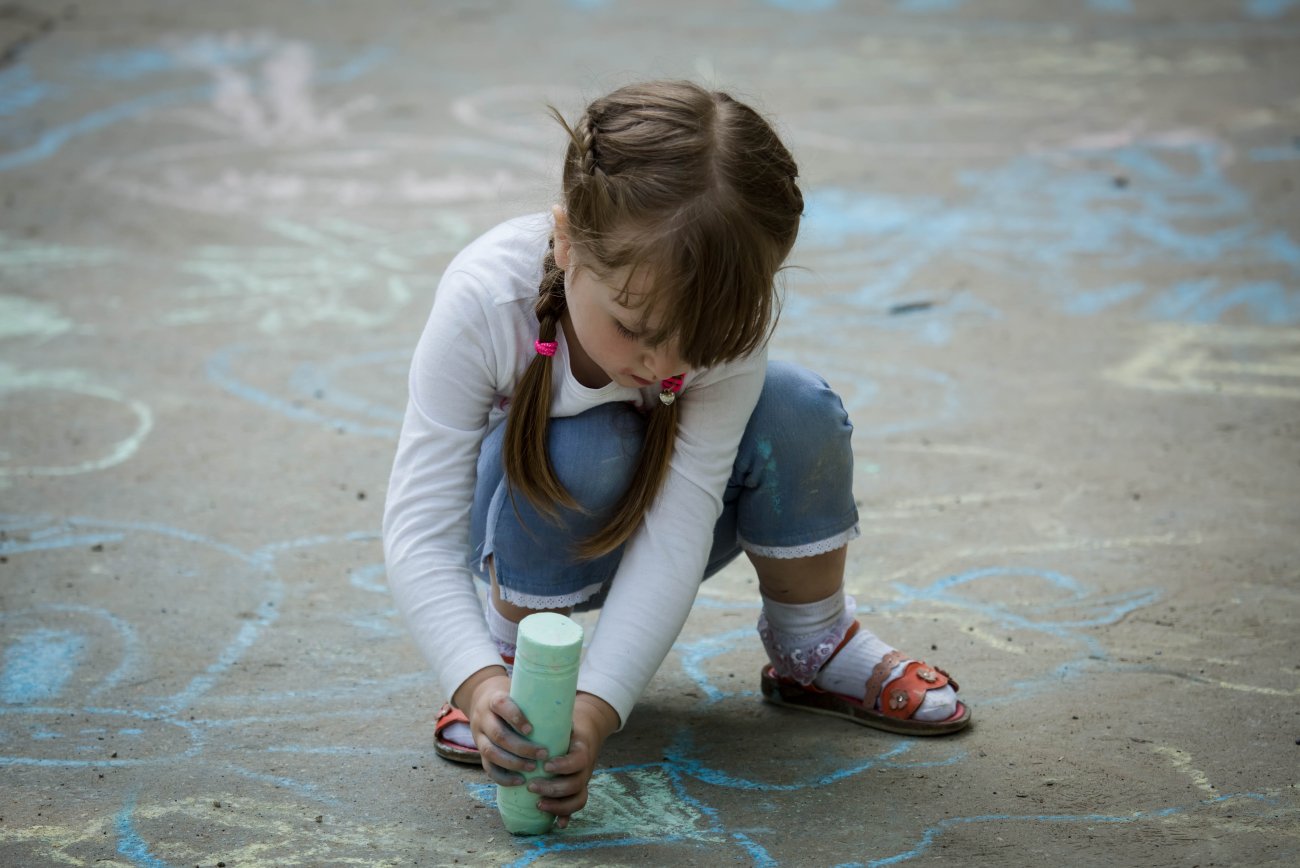 A girl in Moldova draws on the ground with chalk.