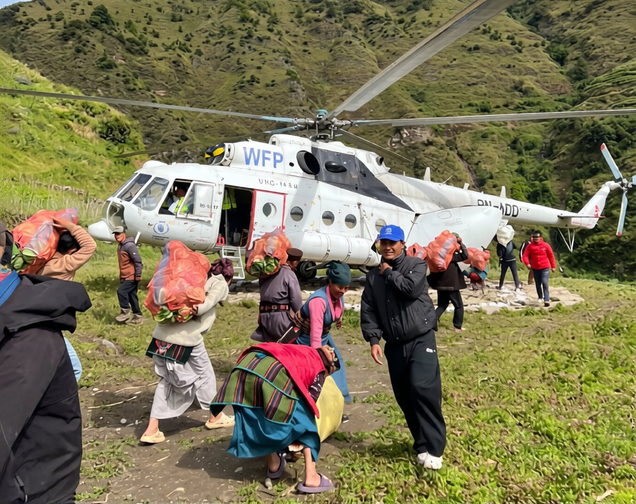 People in Nepal carry bags of food in front of a helicopter.