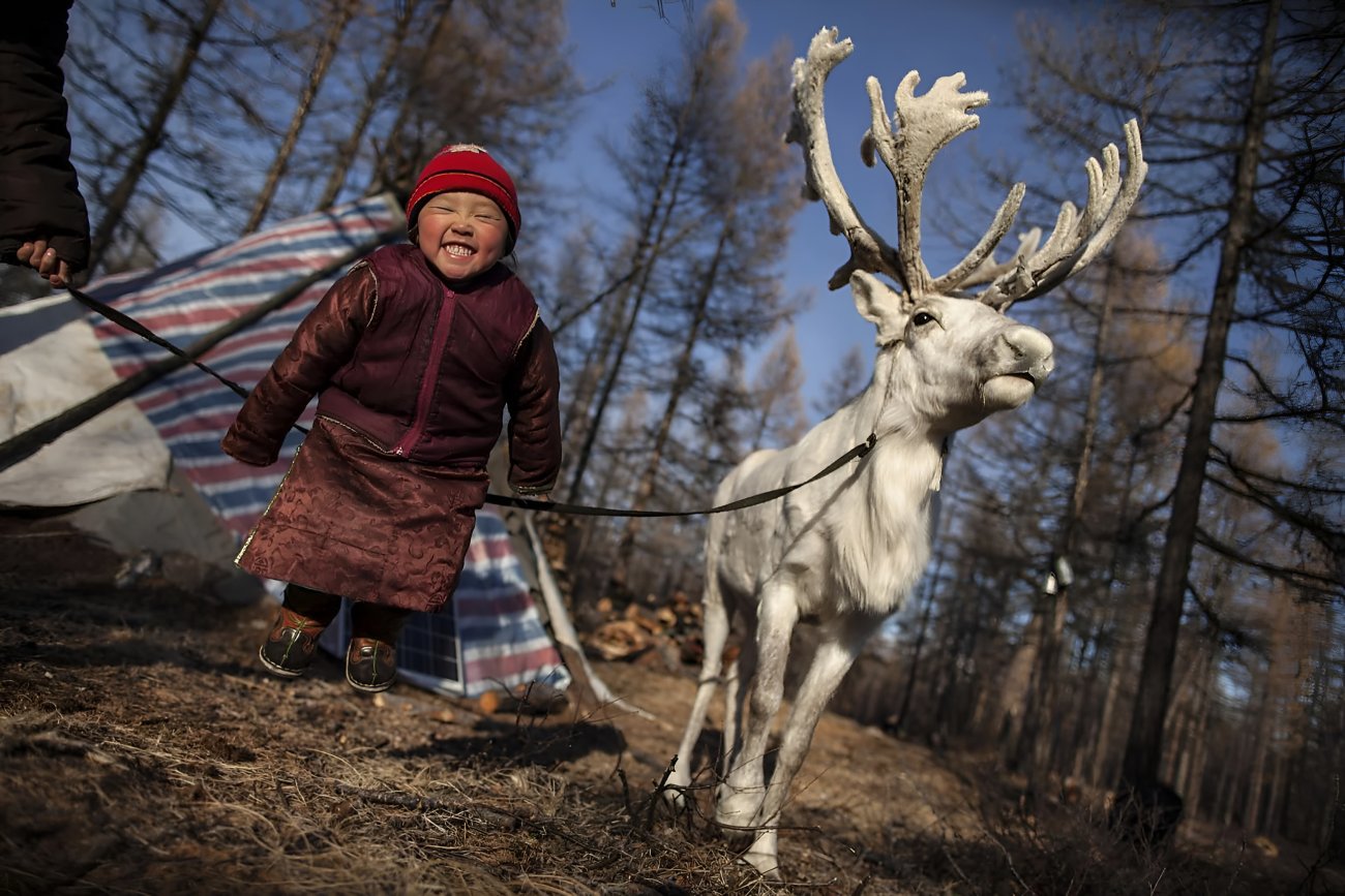 A girl in Mongolia happily smiles next to a reindeer.