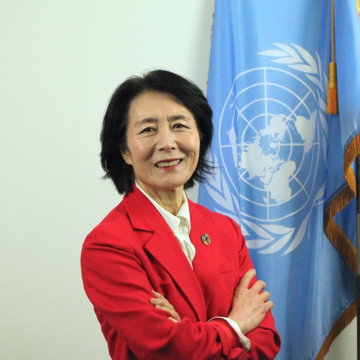 A woman in a red suit blazer against a blue UN flag
