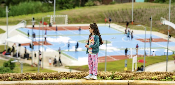 A girl in Costa Rica stands on a hill overlooking a basketball court.