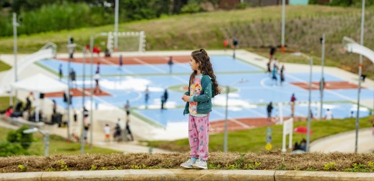 A girl in Costa Rica stands on a hill overlooking a basketball court.