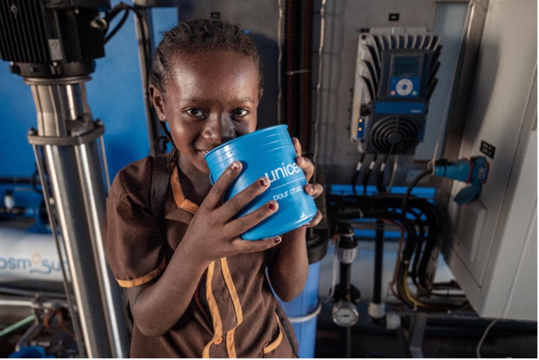 young child drinks water from a blue cup 