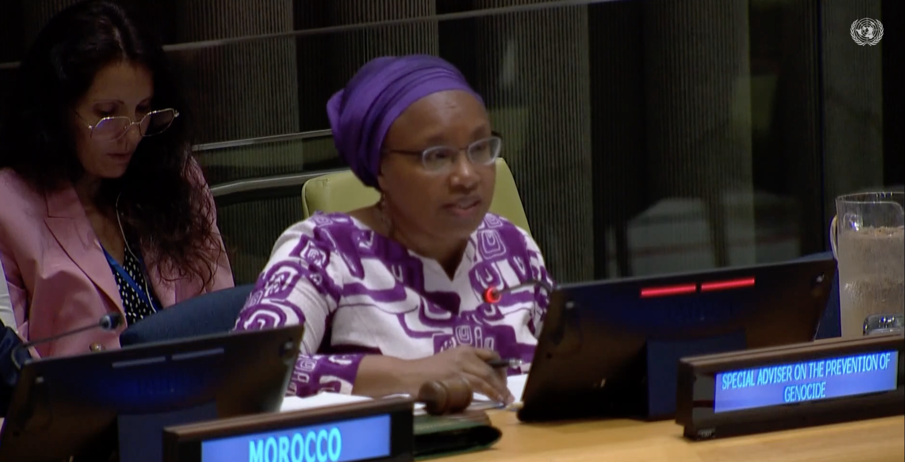 woman in purple dress and head scarf speaks into a microphone in a meeting
