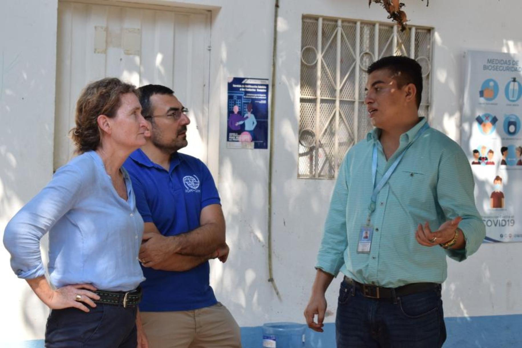 a woman and two men stand speaking to eachother