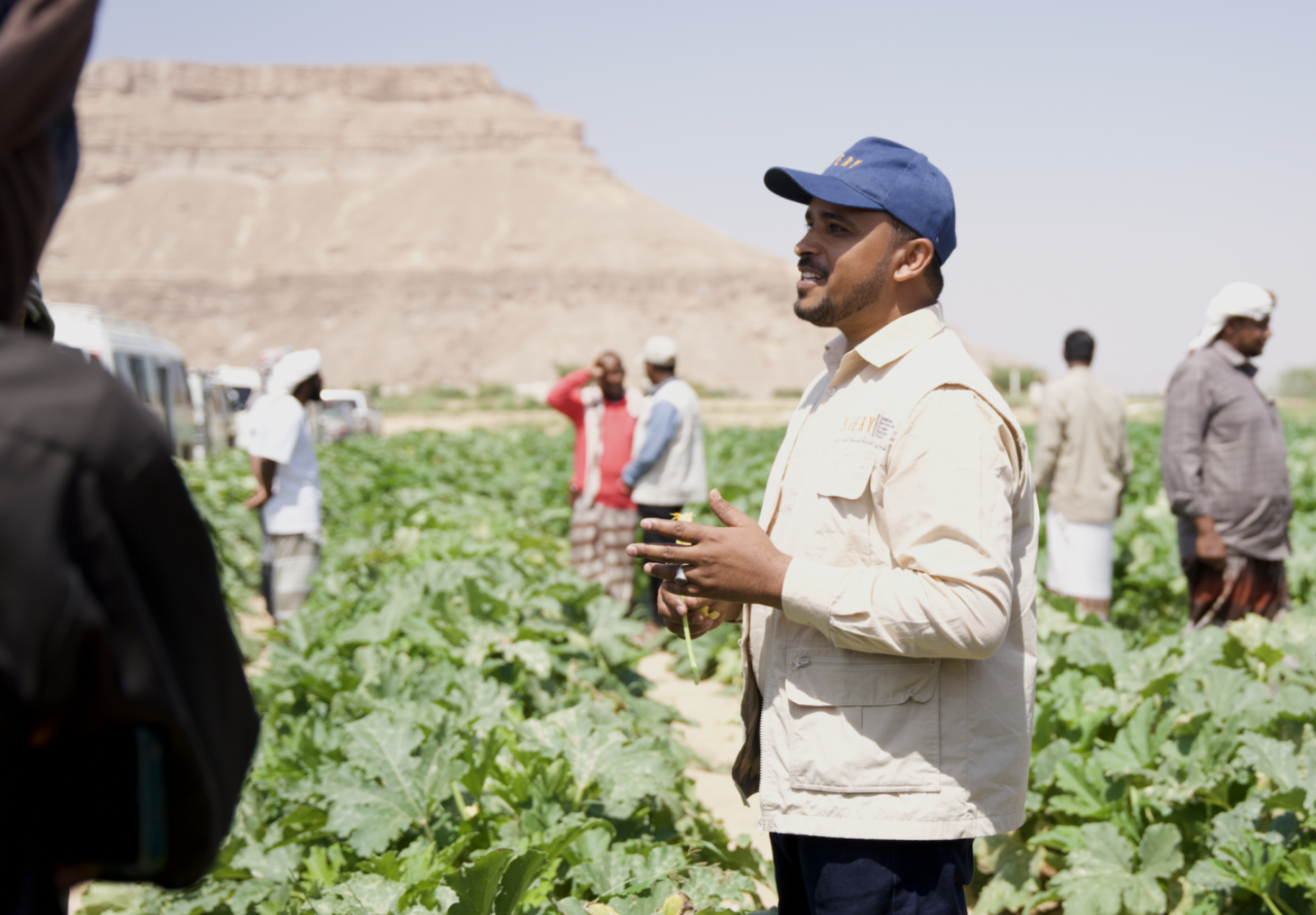 man in white top and blue cap stands in green field with others in the background