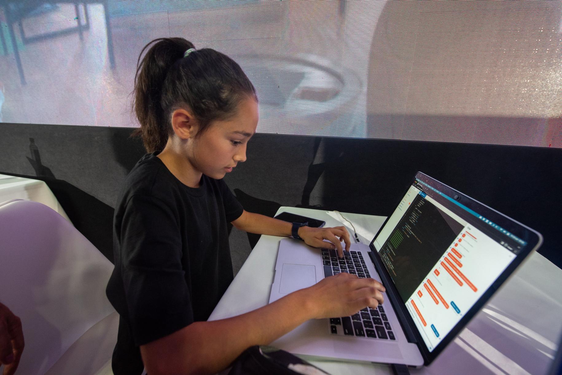 young girl in dark top works on laptop 