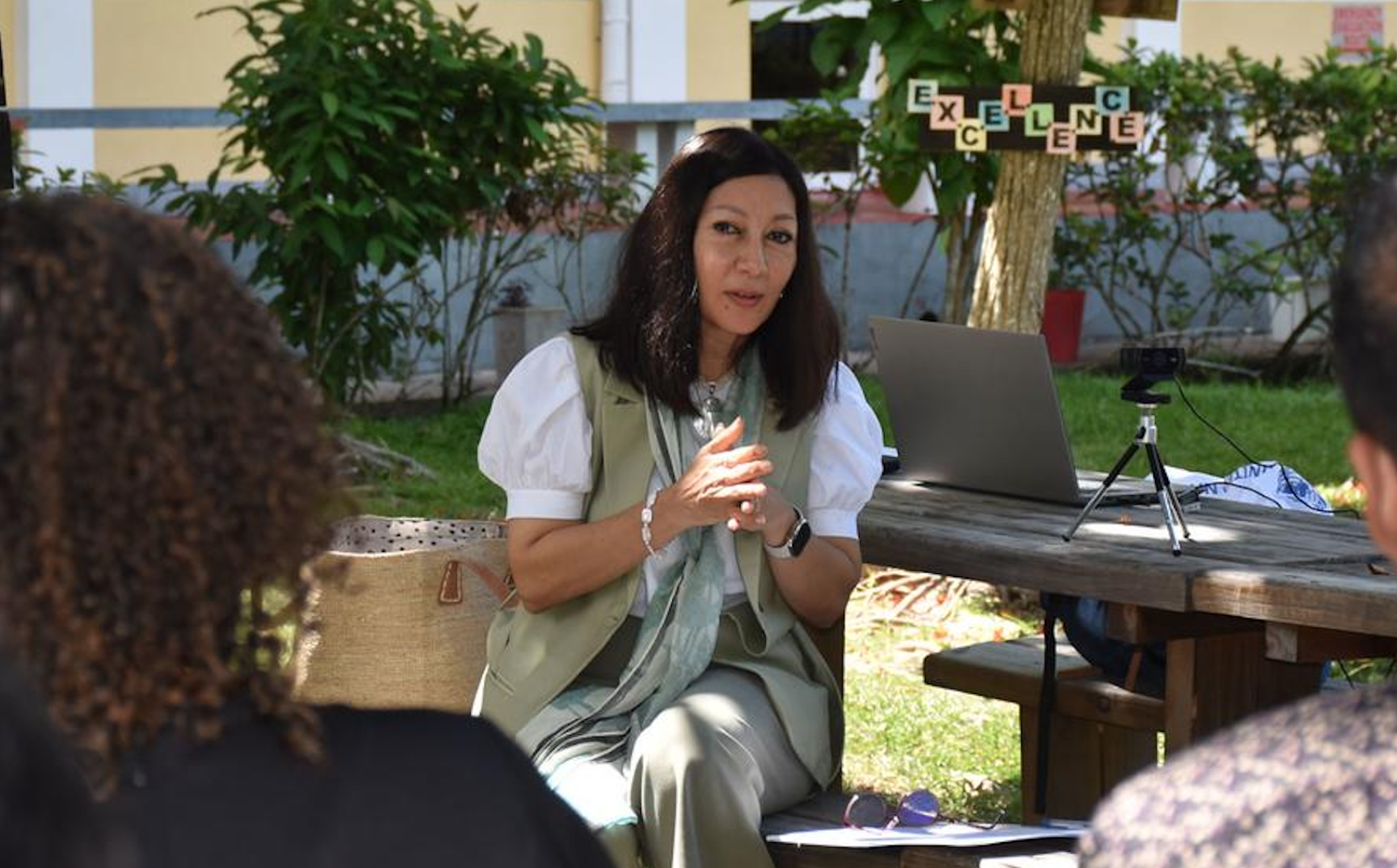 woman with dark hair and white shirt gestures with her hands while speaking to people in front of her