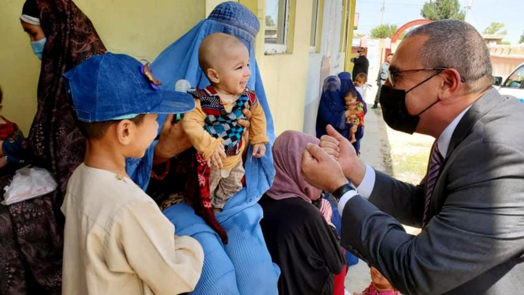 man in dark and face mask kneels down to speak to child wearing blue cap