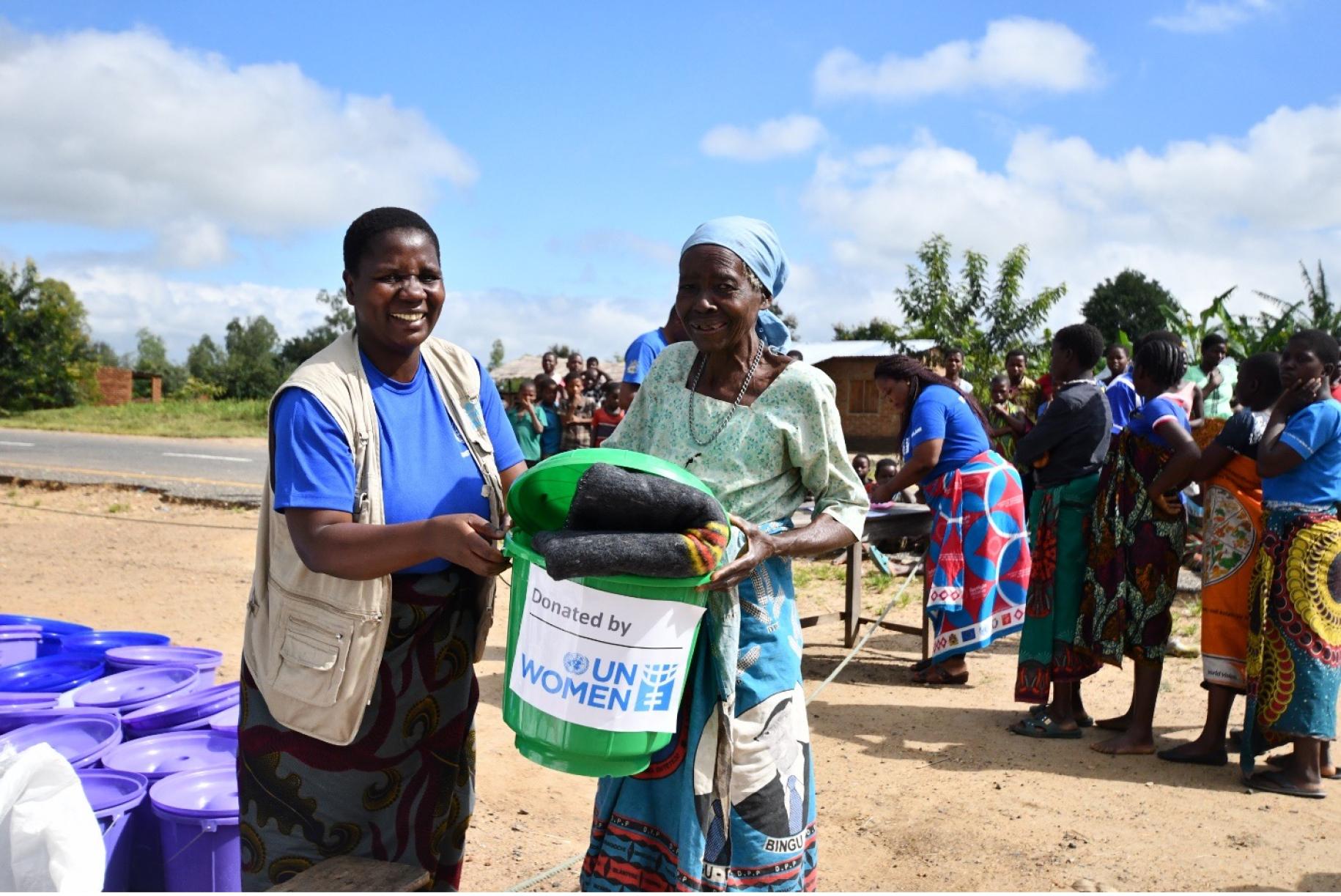 two women stand holding a green bucket with a blanket in it