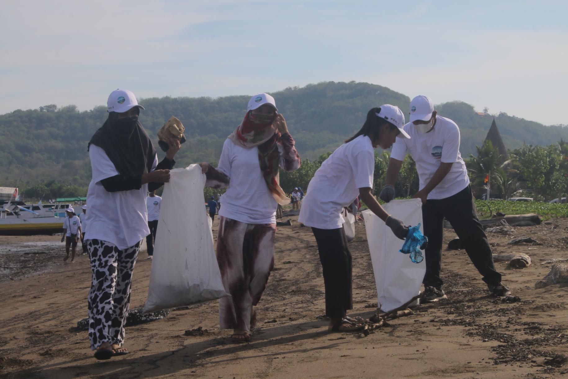 Four people in white shirts and hats clean up a beach with giant white bags of trash