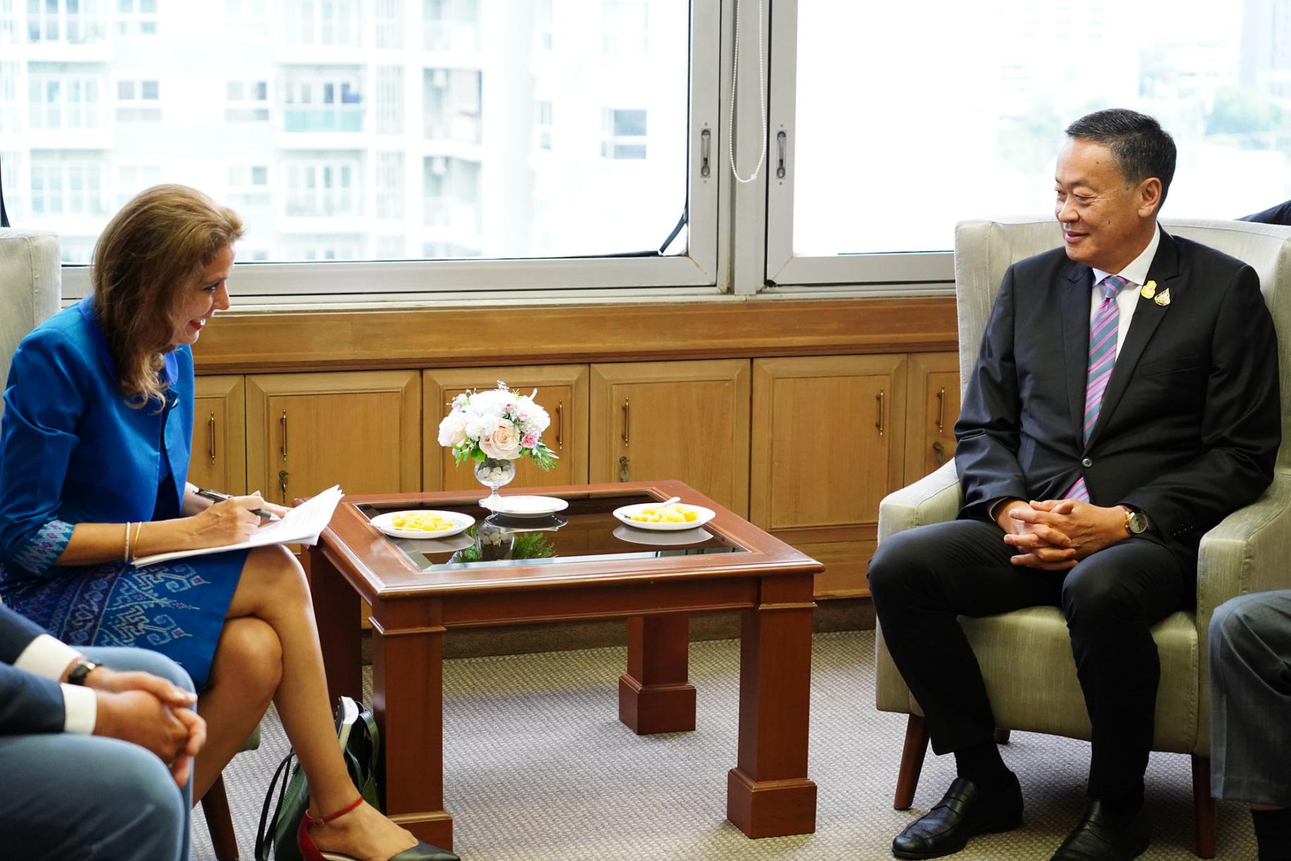 woman in blue suit sits opposite man in dark suit speaking 