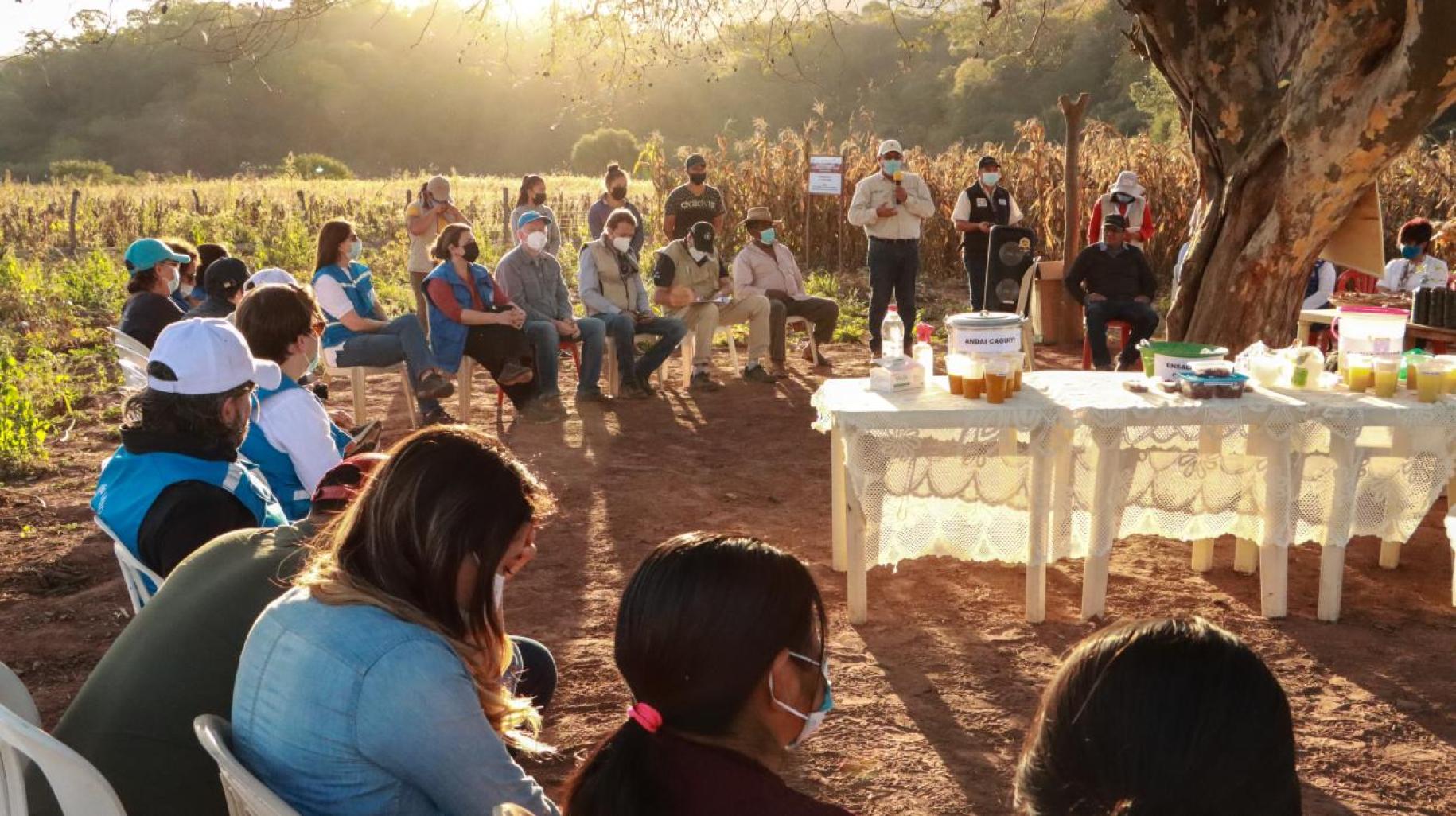 group of people sitting in a circle on chairs outside as the sun sets