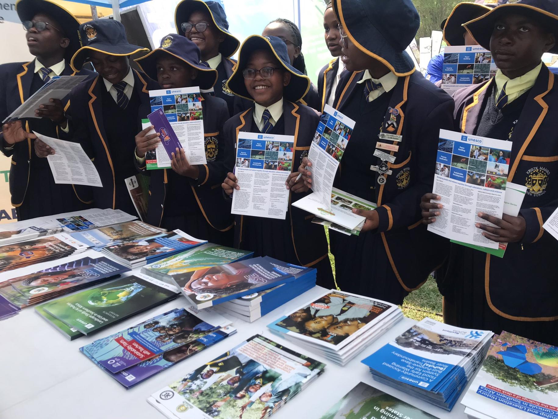 group of school children in uniforms hold up booklets and smile to the camera