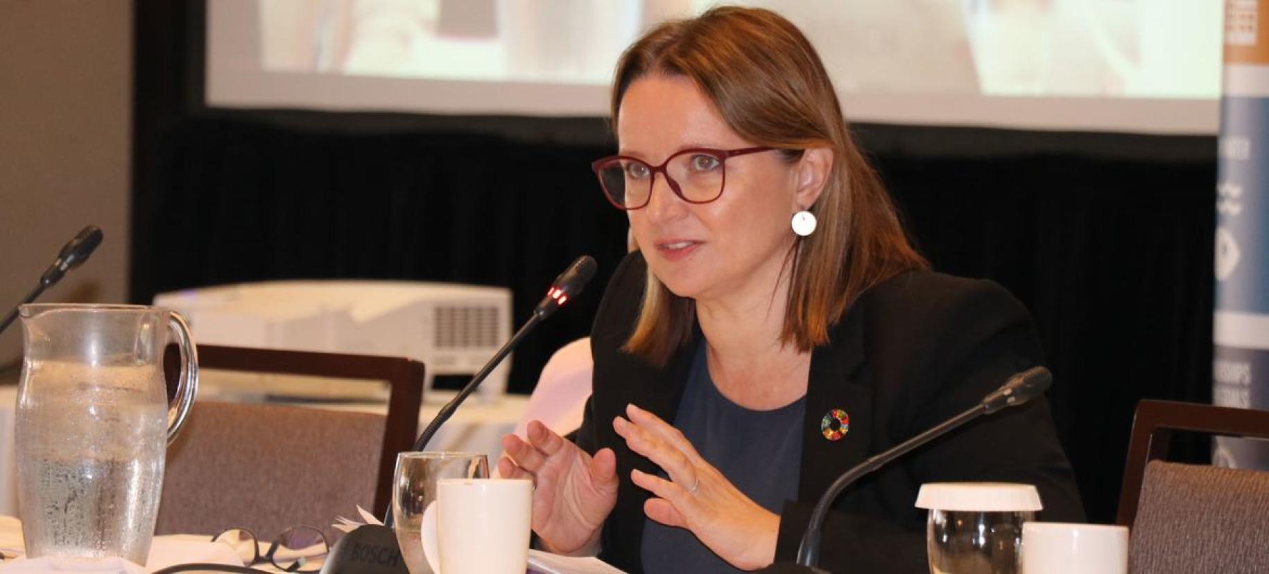 woman in dark suit speaks in front of screen