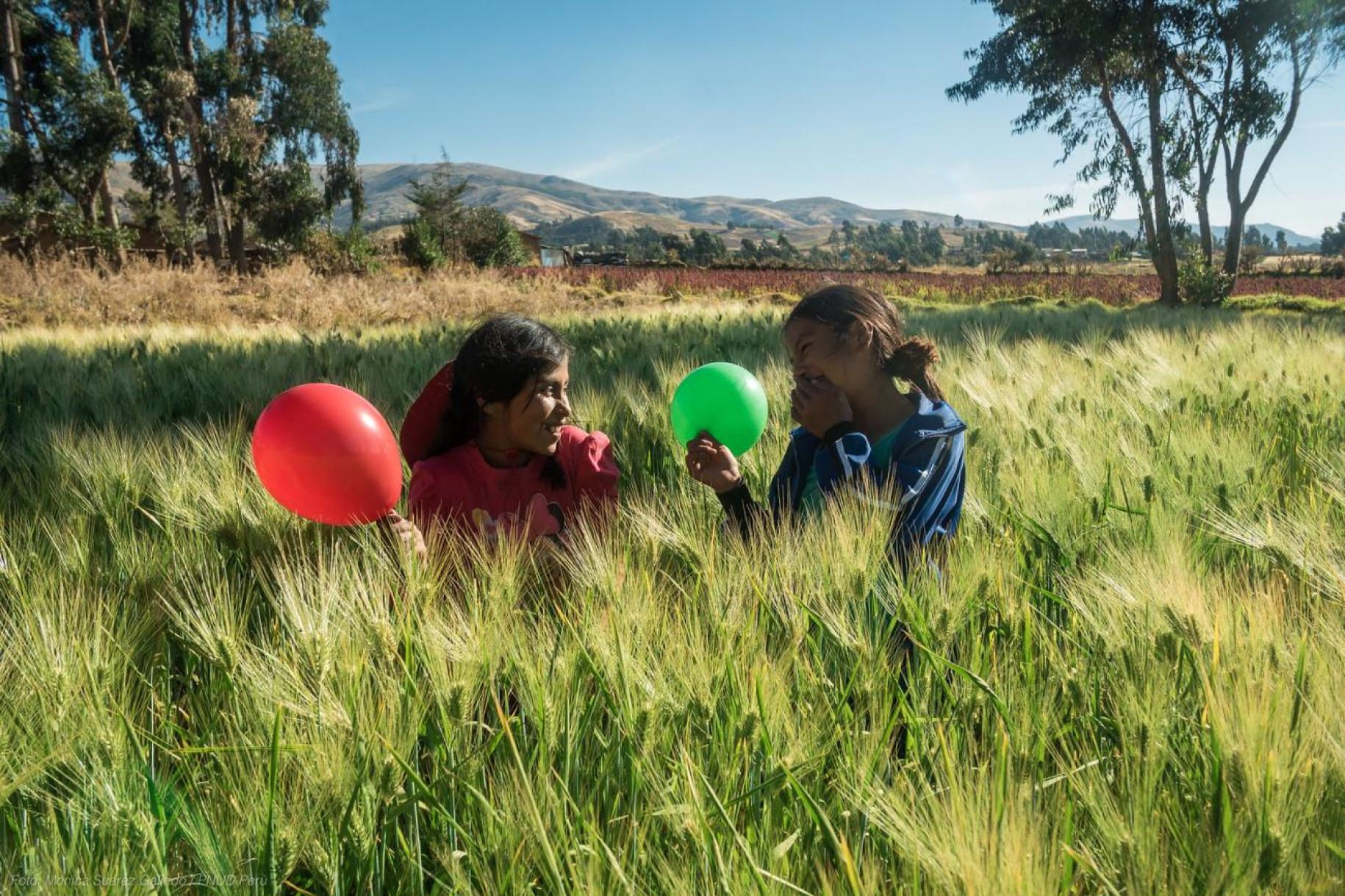 two young children sit in green field holding balloons