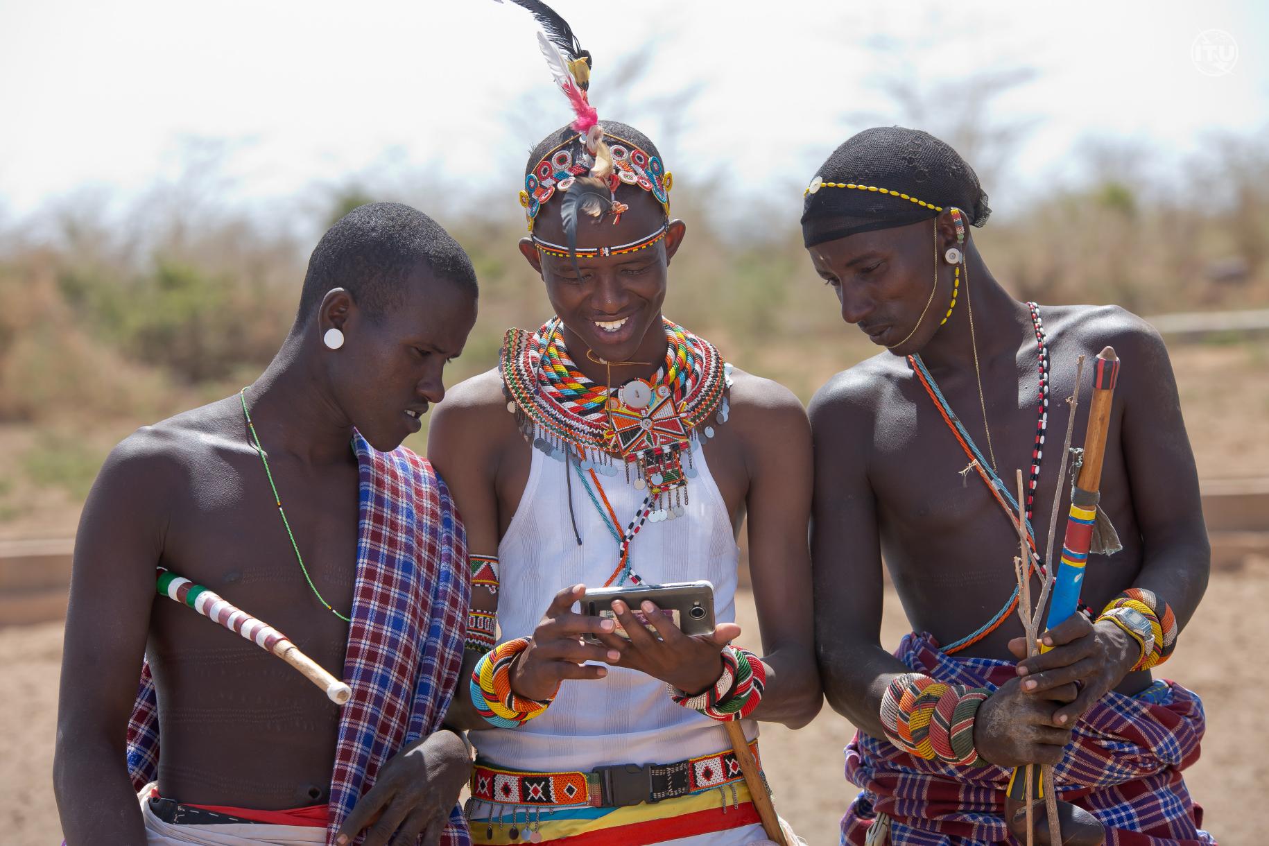 three men in traditional Kenyan dress look at mobile phone 