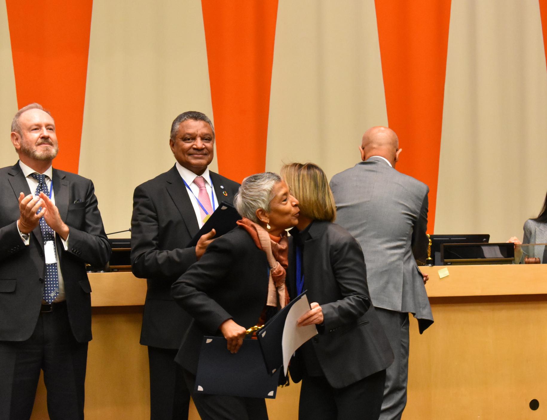 two women in suits hug on stage wile receiving an award 