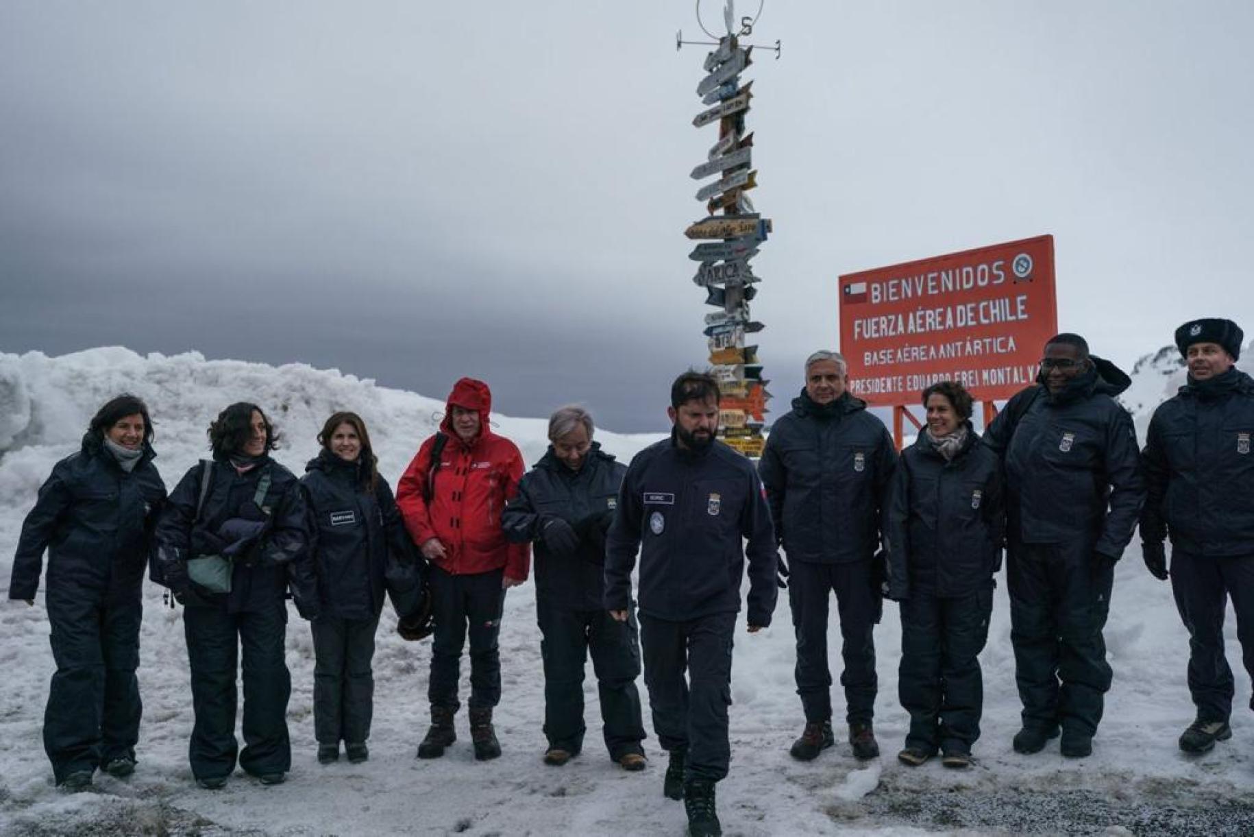group of people stand on ice covered ground with red sign behind them 