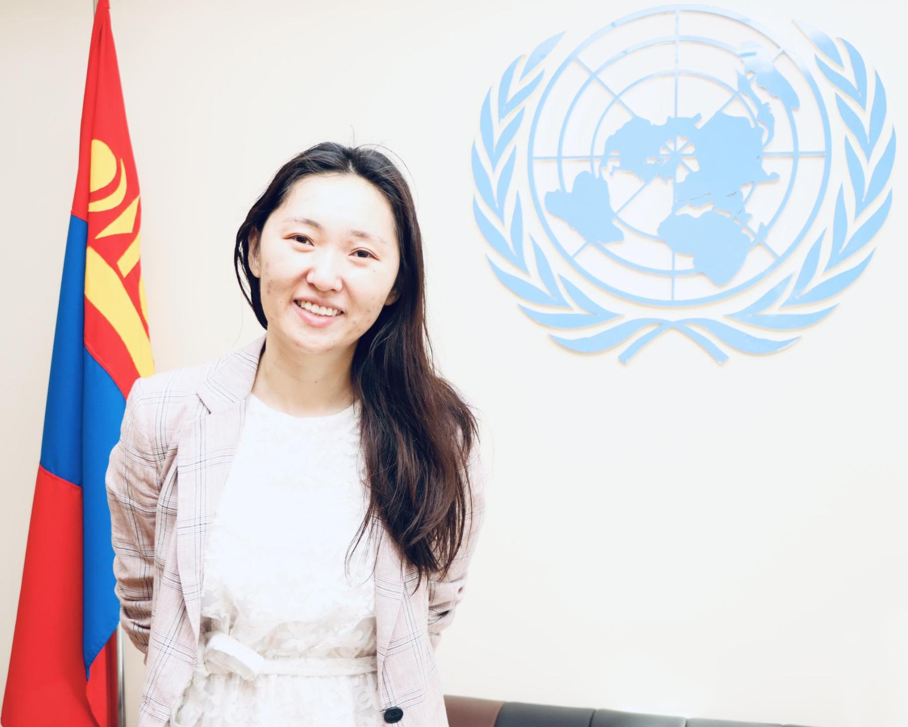 Suvd Bold standing in front of the UN logo with a flag of Mongolia by her side