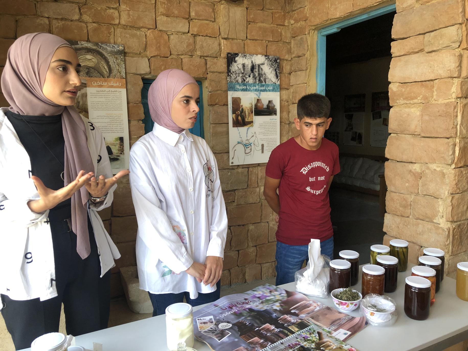 two young woman and a man stand behind stall showing their products