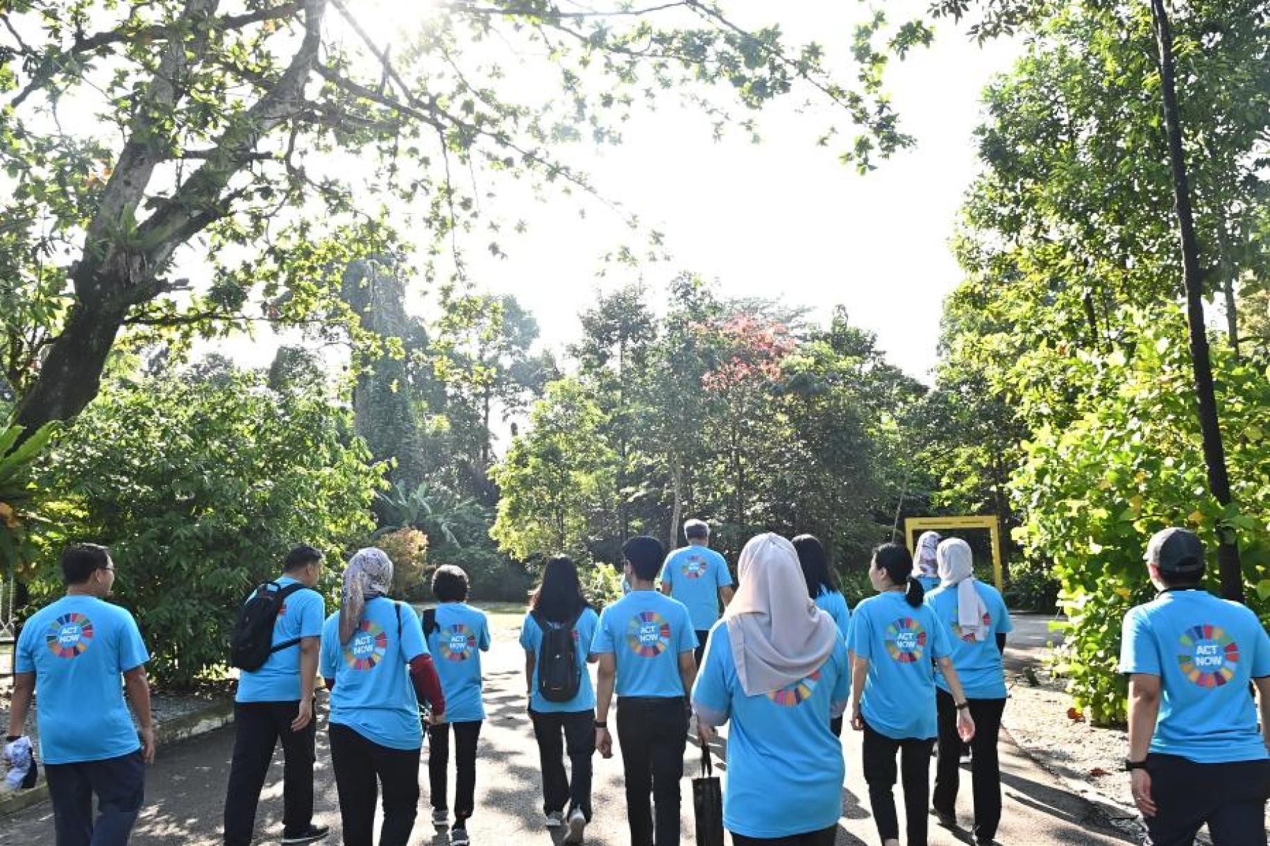 group of people in blue t-shirts walking with their backs turns towards trees