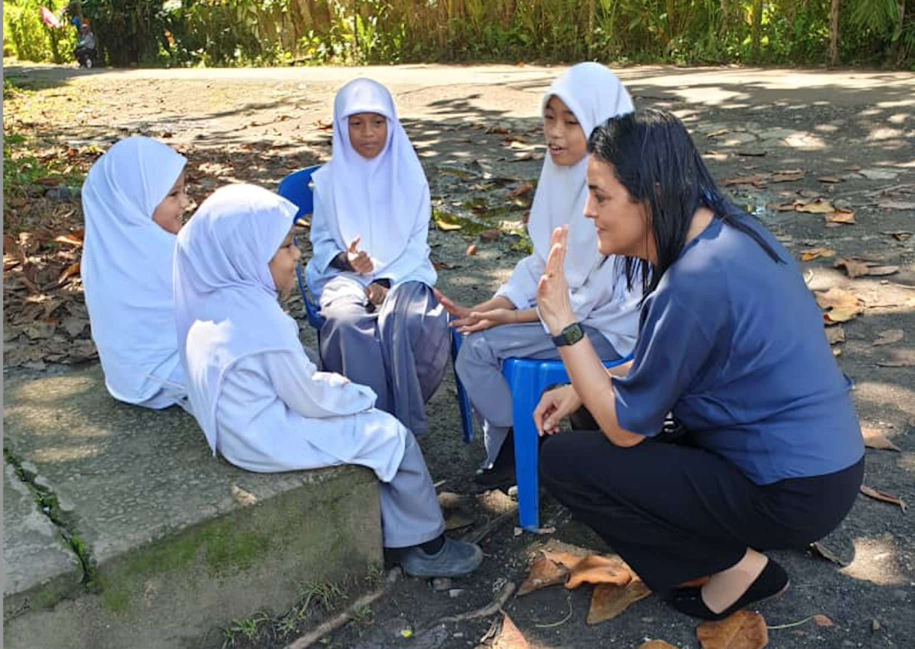 young children in white headscarves speaks with a woman leaning down on one knee