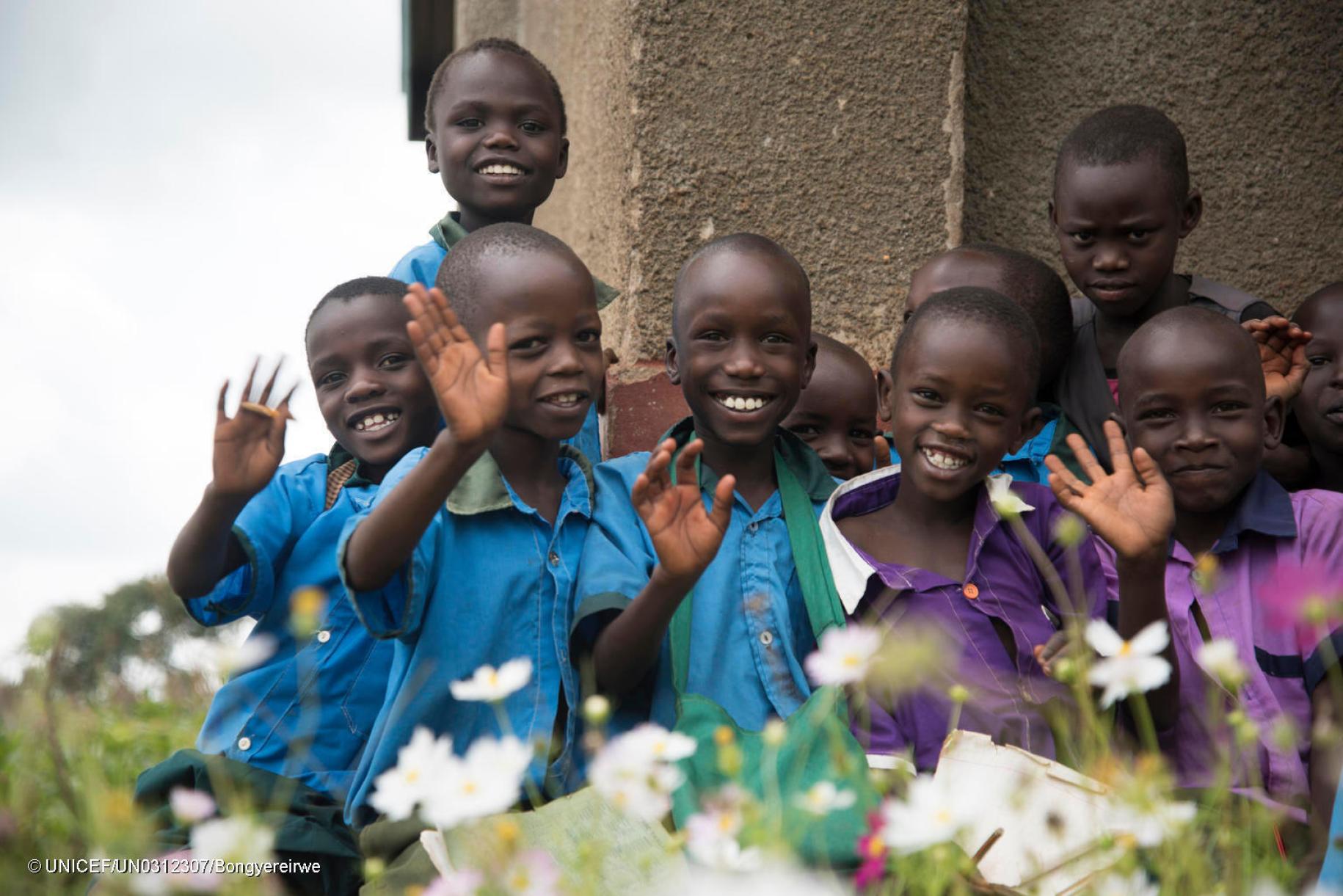 group of young school boys in blue and purple shirts stand together and wave at the camera