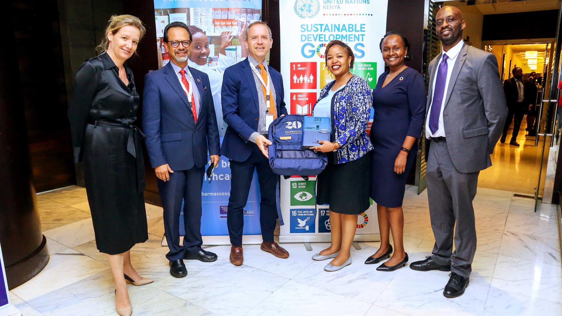 group of men and women in suits stand in front of poster displaying UN SDG logos