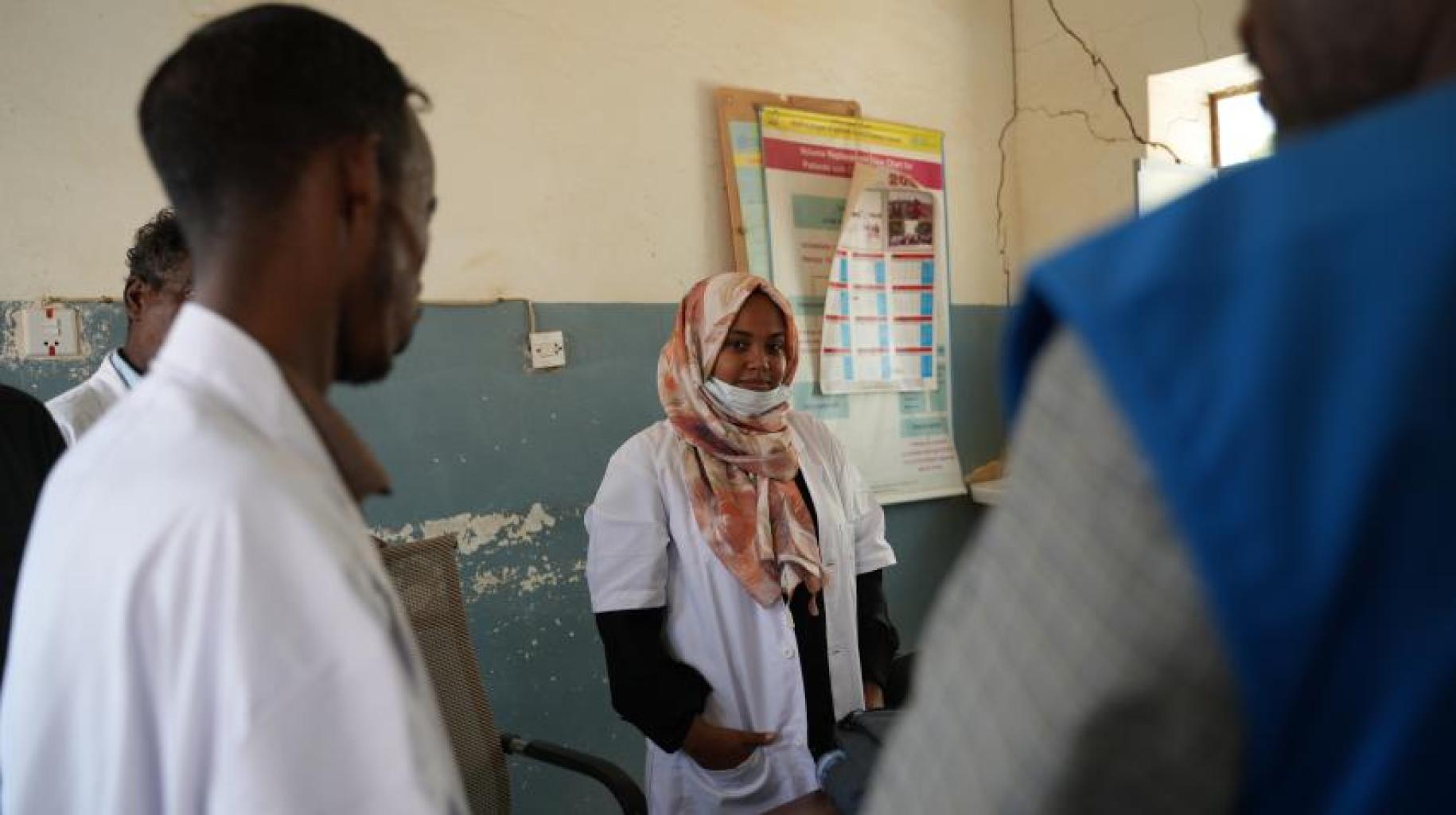 A view of a group of doctors and nurses in white lab coats speaking at a clinic in Sudan. 