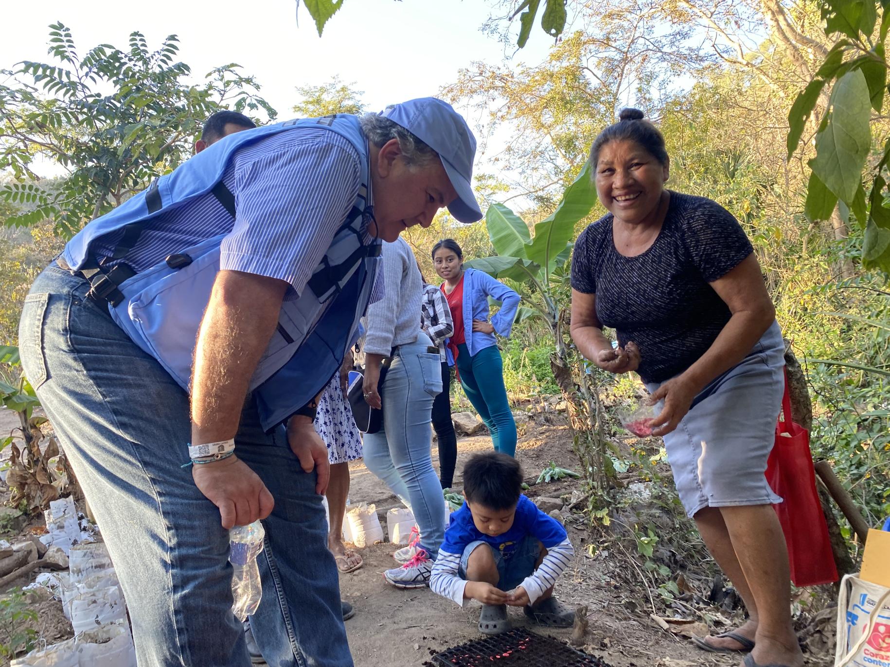 A man leans over as a woman and her child plant a tree