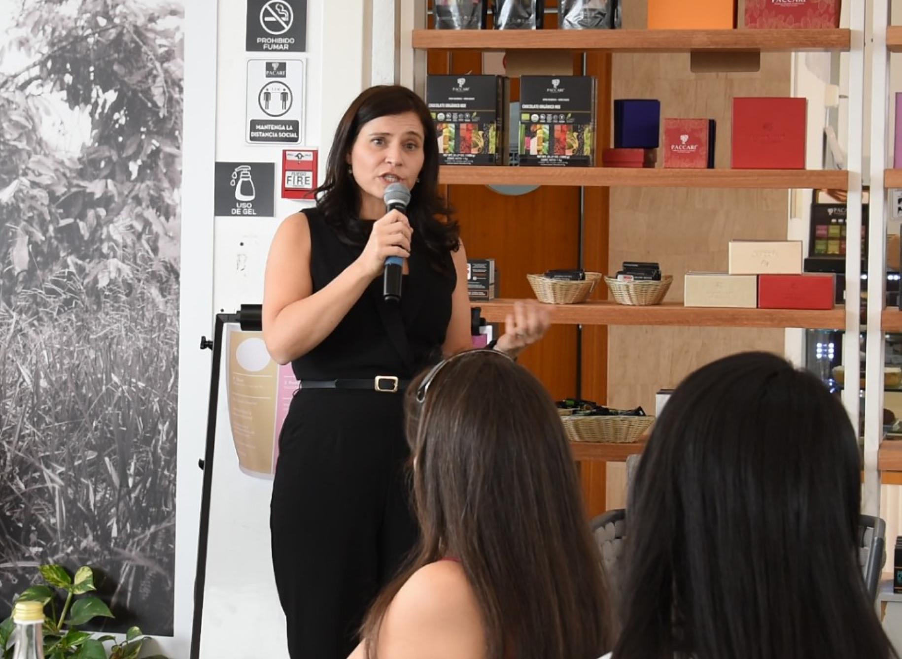 A woman in a black dress speaks into a microphone while other women listen to her