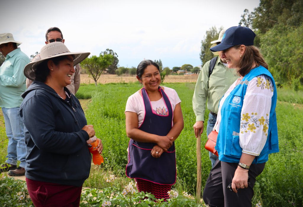 A small group of people stand together in a green agricultural field, engaged in conversation.