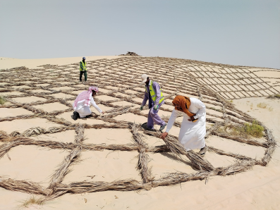Men wearing white tunics and headscarves working in adesert.